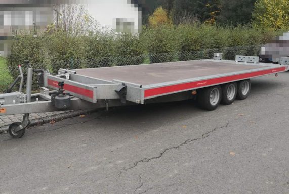 Ein großer, roter Anhänger mit drei Achsen, auf einer Straße geparkt.