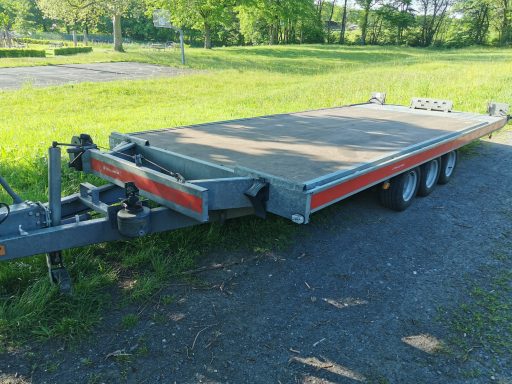 Zwei Achse Anhänger Autotransporter Flacher Anhänger mit einer großen Ladefläche, auf einem grünen Rasenparkplatz.