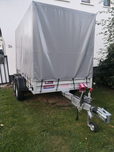 Rückansicht eines Anhängers mit grauer Plane auf grünem Gras.